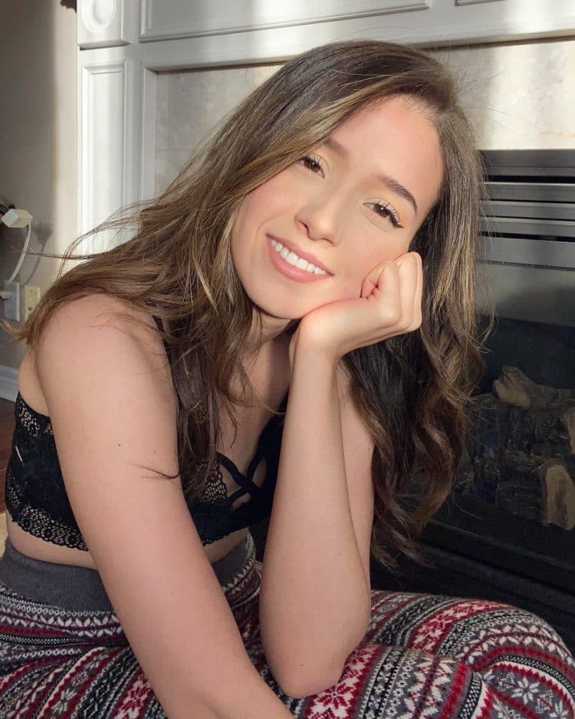 Pokimane poses in front of a fireplace.