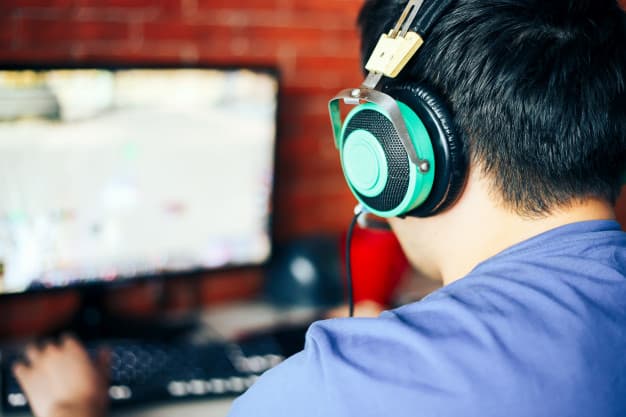 Photo of a teenager with headphones playing a PC game.