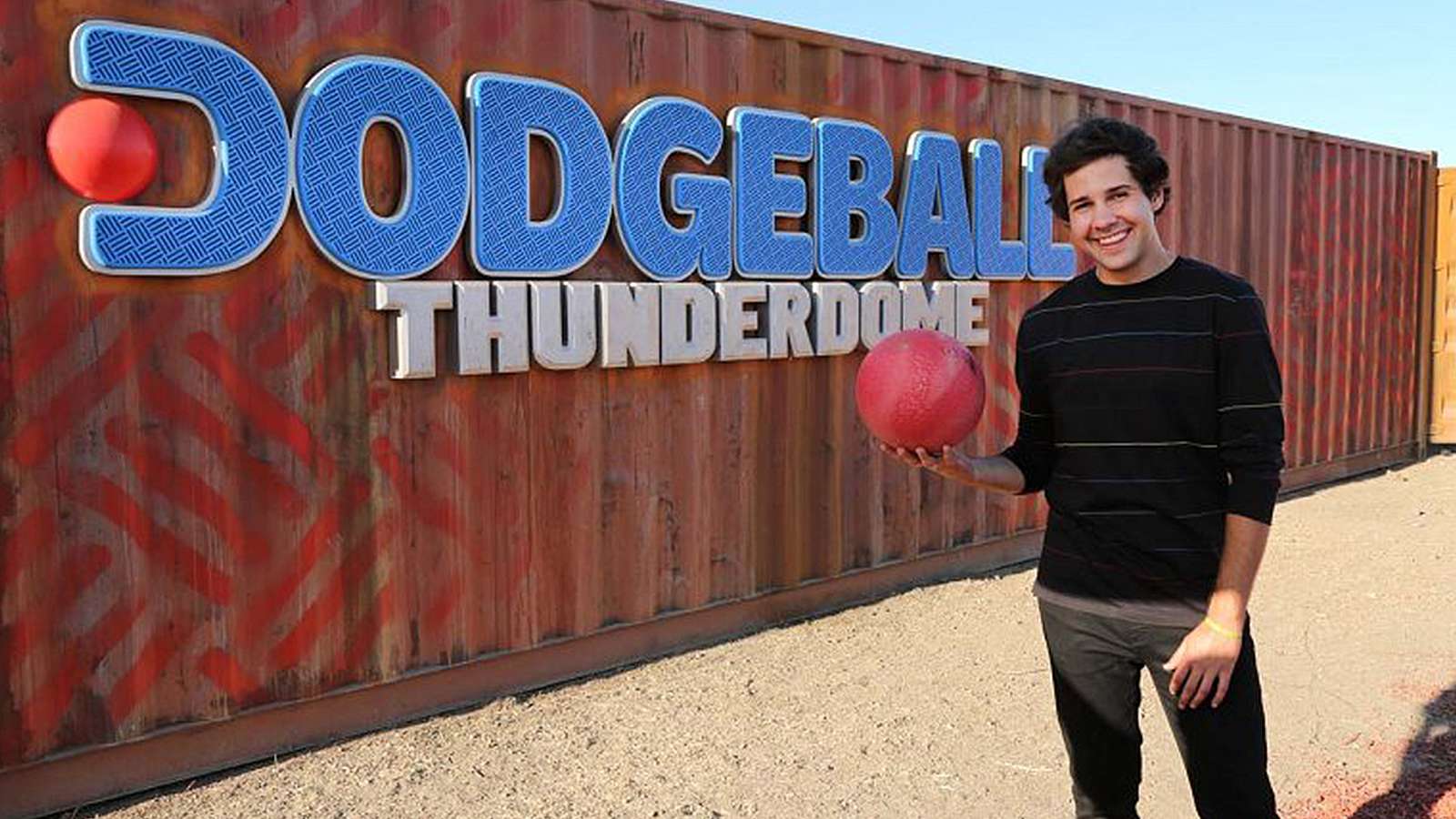 David Dobrik stands next to a metal shipping container with the words "Dodgeball: Thunderdome"