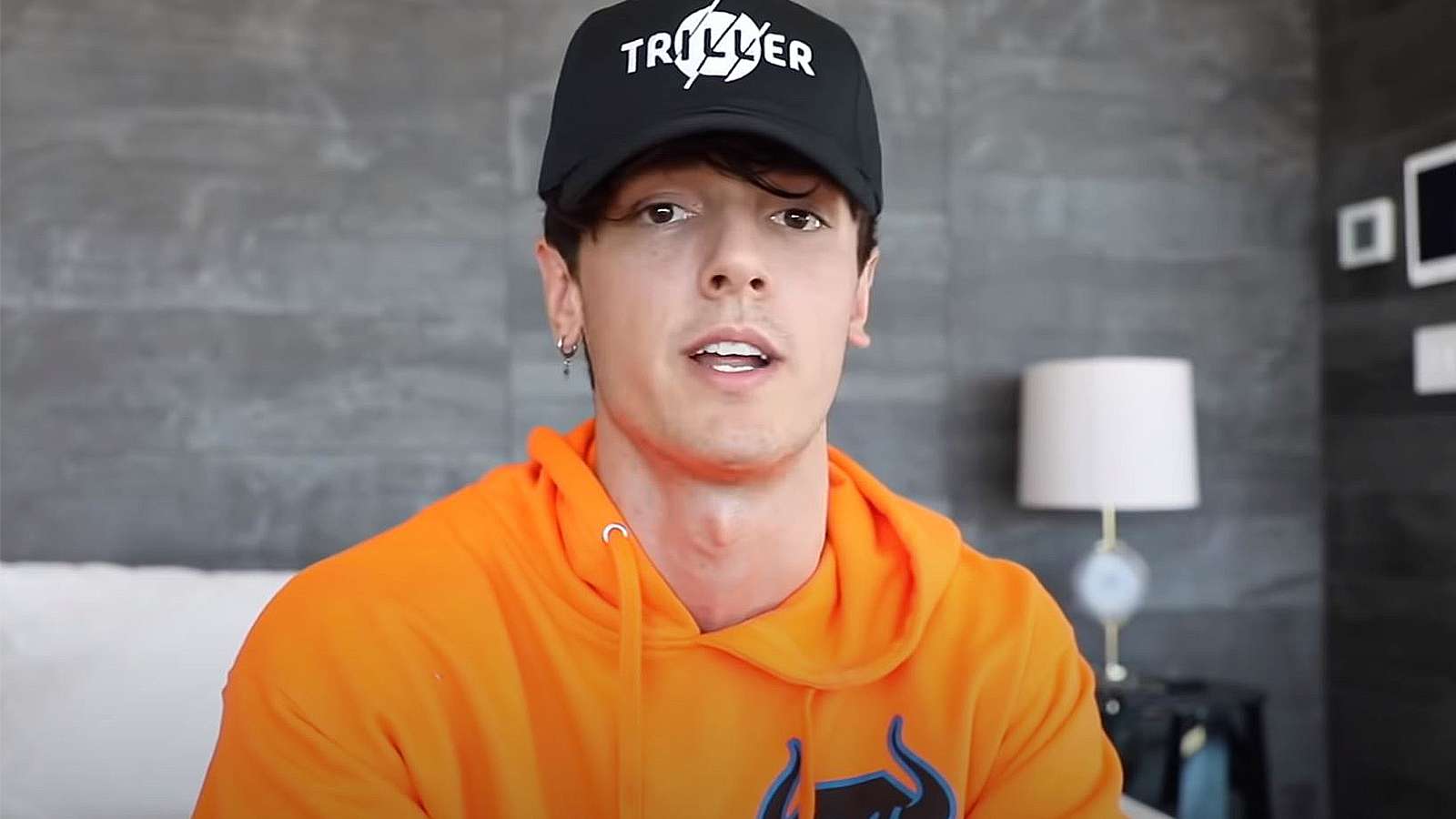 Bryce Hall speaks to the camera wearing an orange hoodie and black baseball cap.