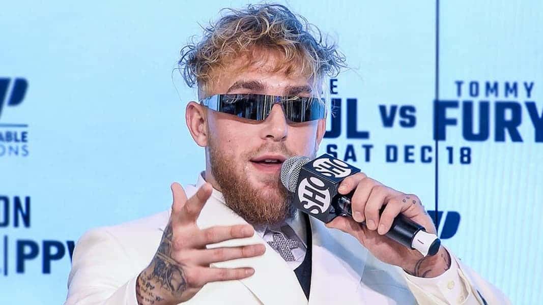 Jake Paul in white suit and sunglasses holding microphone