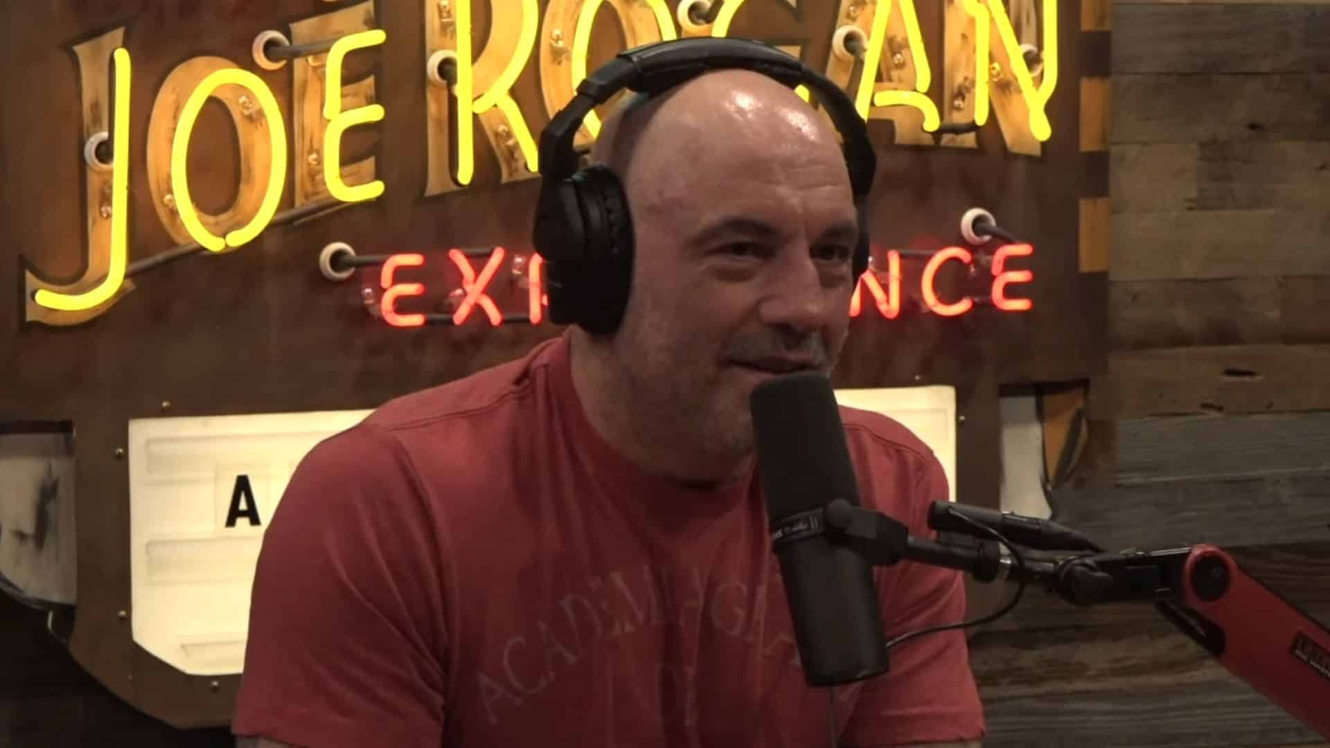 Joe Rogan in red shirt in podcast studio talking into mic