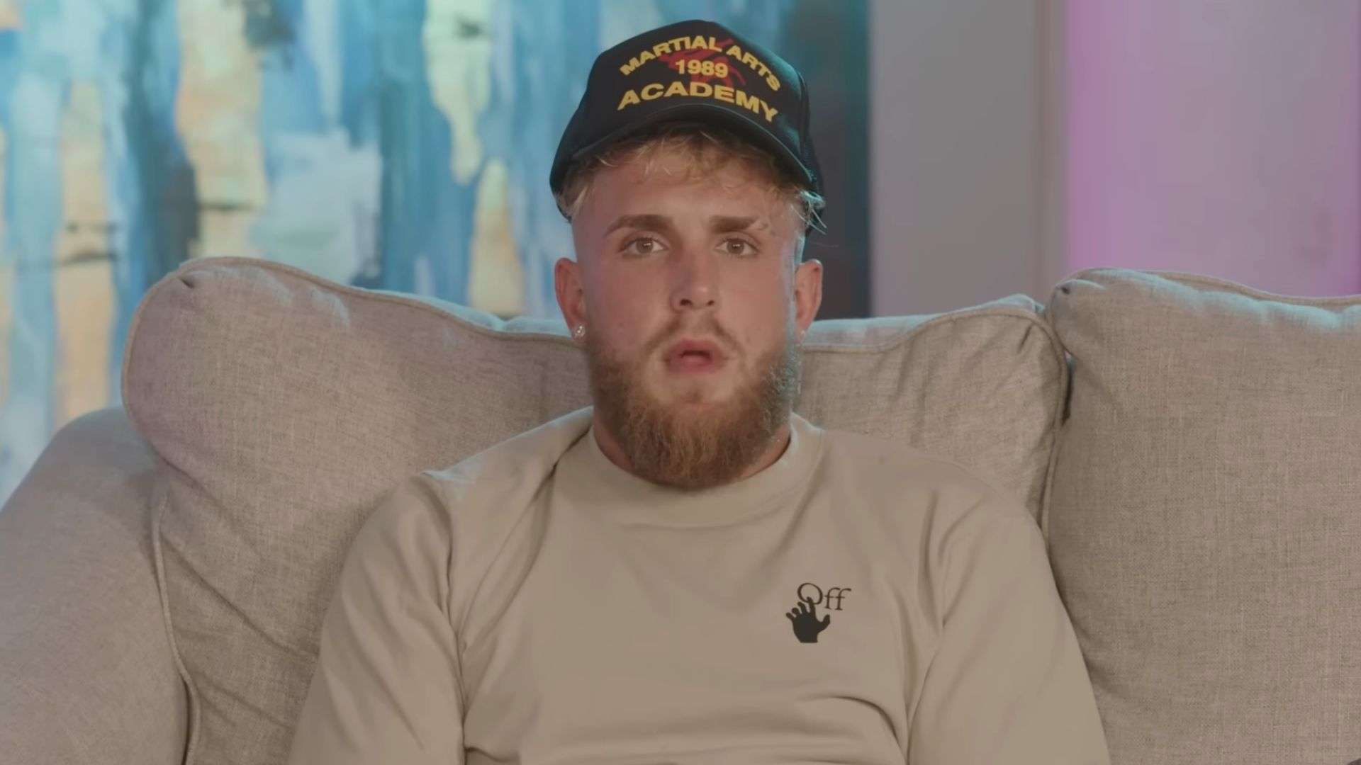 Jake Paul sitting on sofa talking to camera in hat and t-shirt