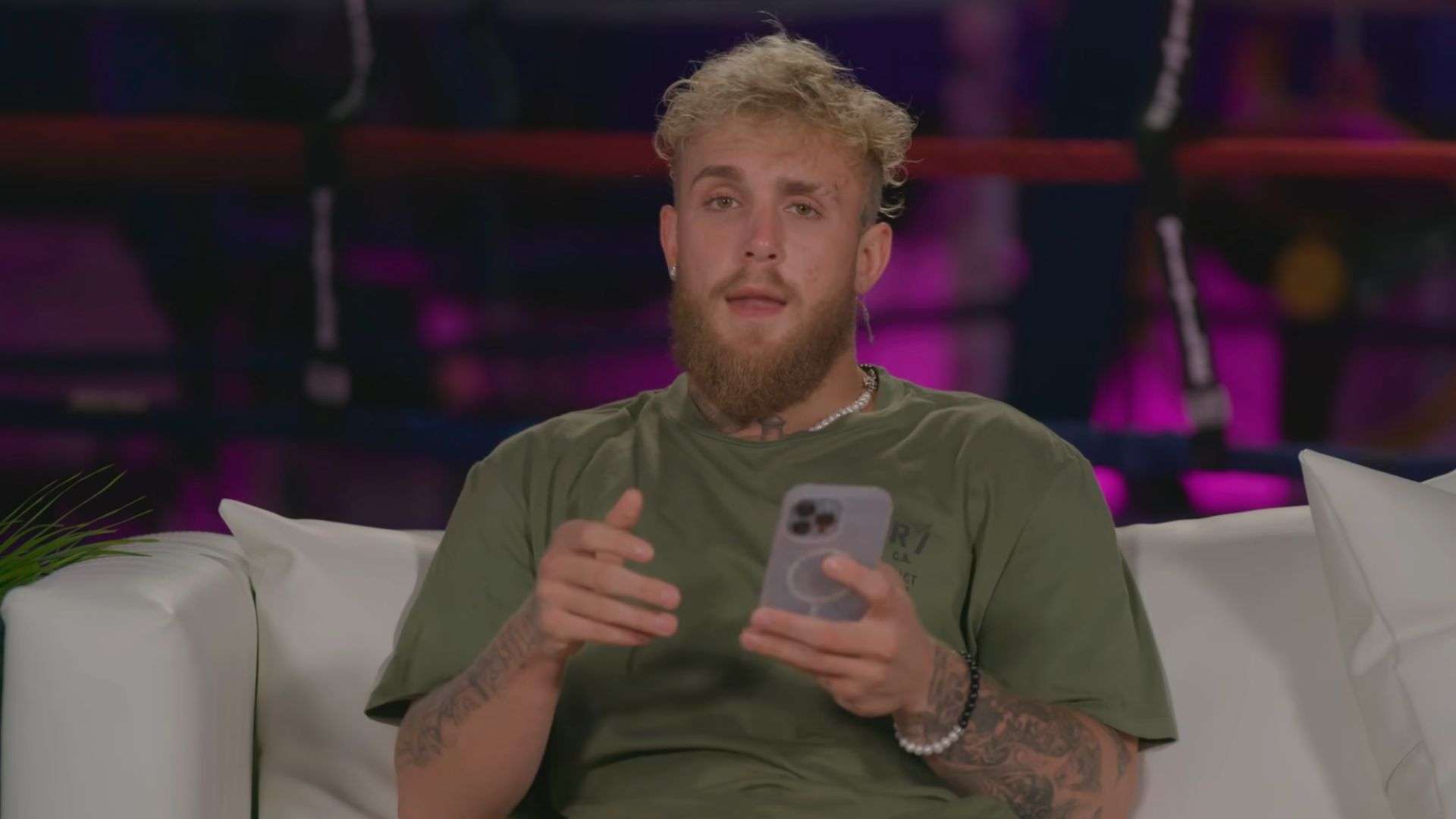 Jake Paul talking to camera with phone in hand on couch