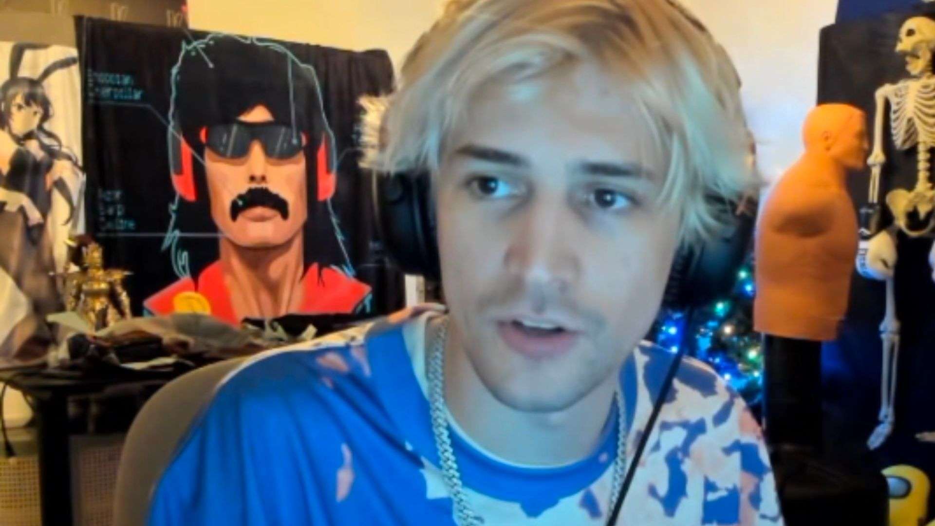xQc in blue and white shirt in front of dr disrespect blanket looking at camera