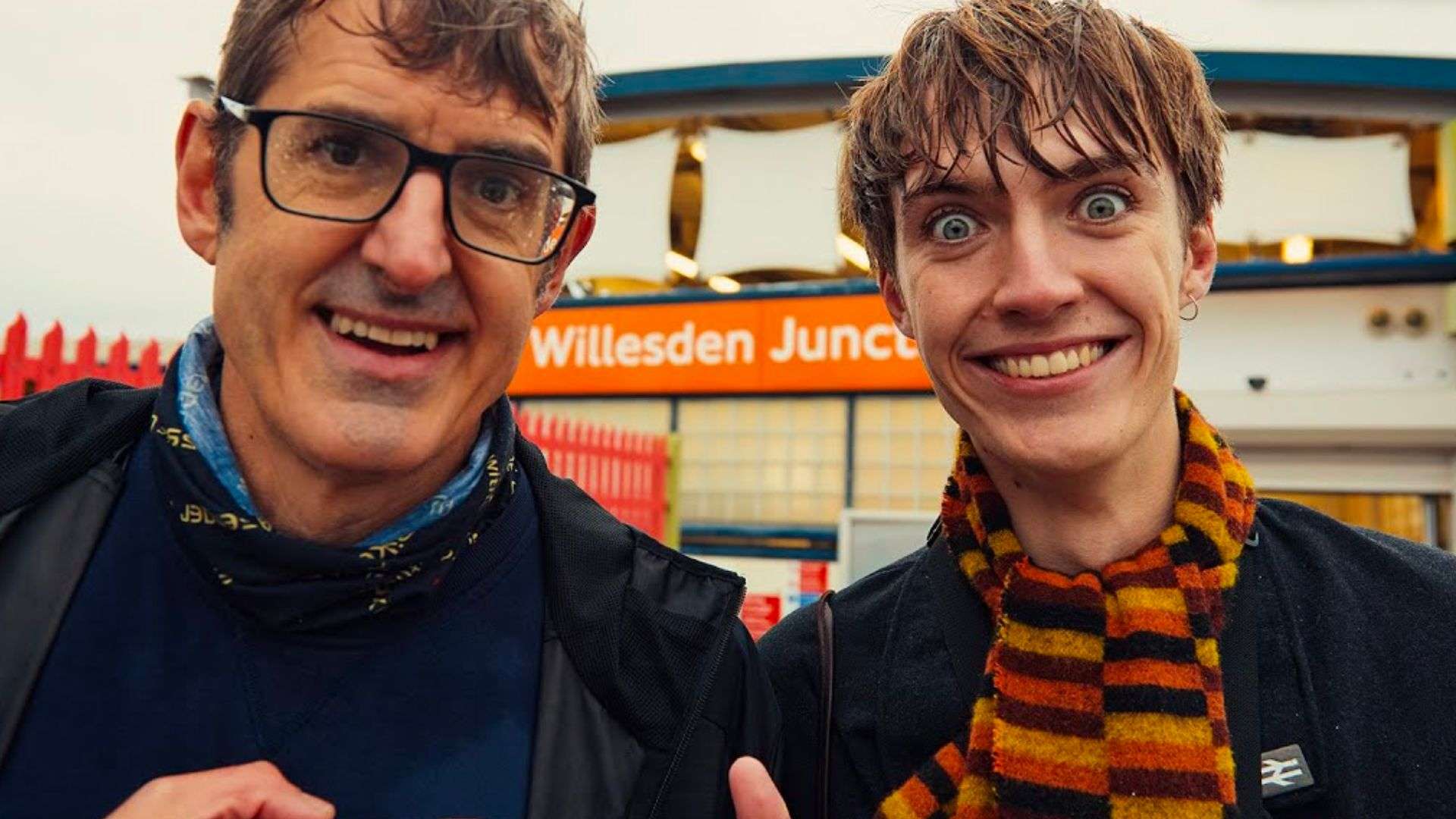 Francis Bourgeois and Louis Theroux outside train station smiling covered in rain