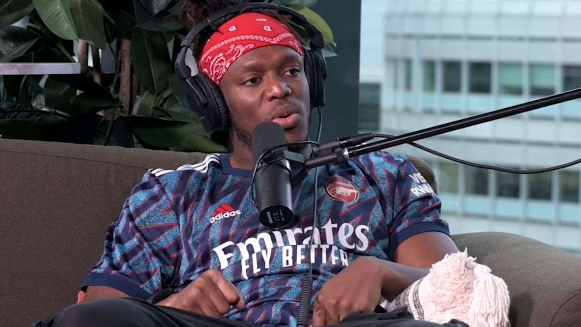 KSI in red bandana and purple arsenal shirt talking into microphone