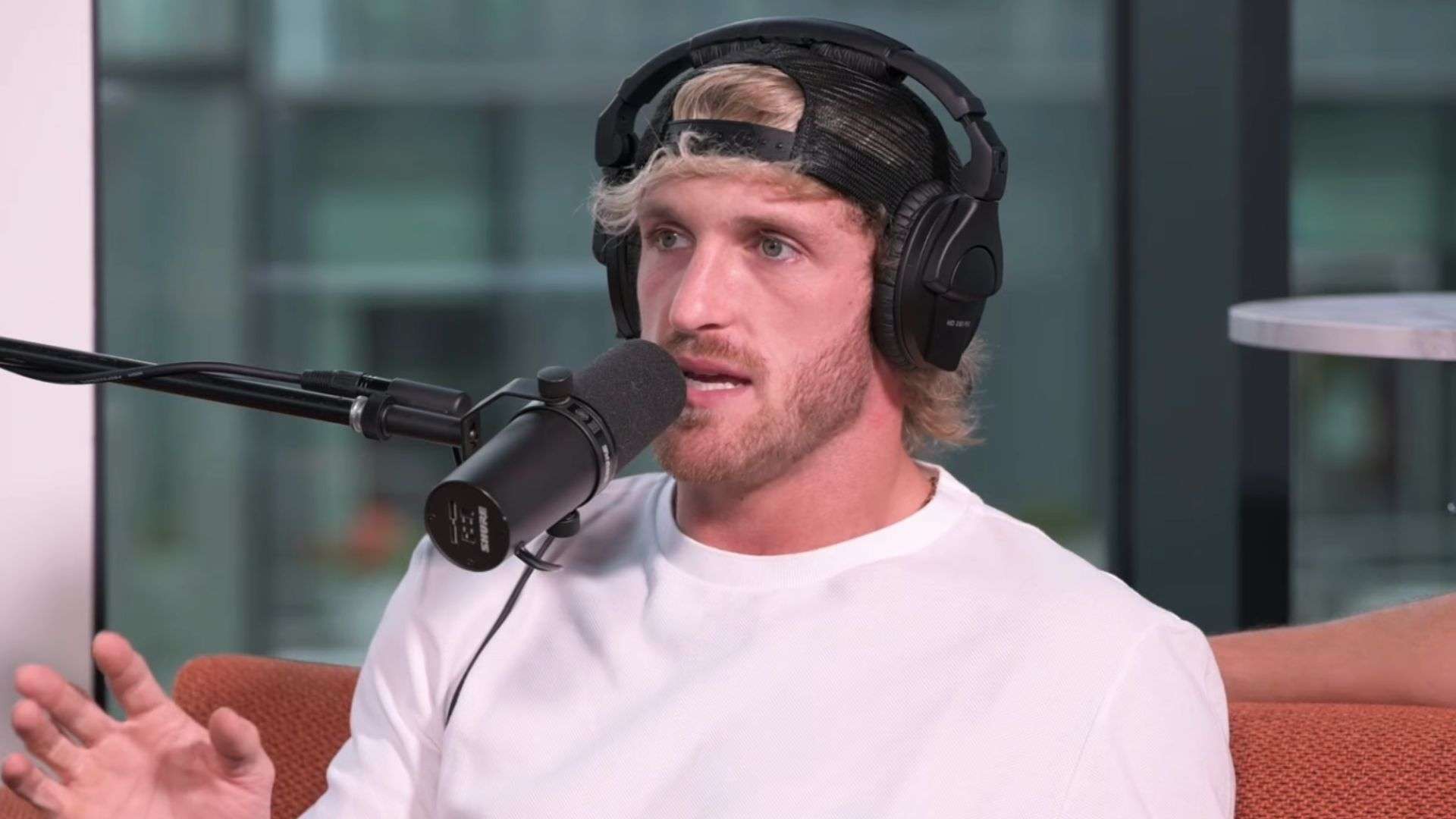 Logan Paul in white shirt and backwards hat sat on couch talking into mic