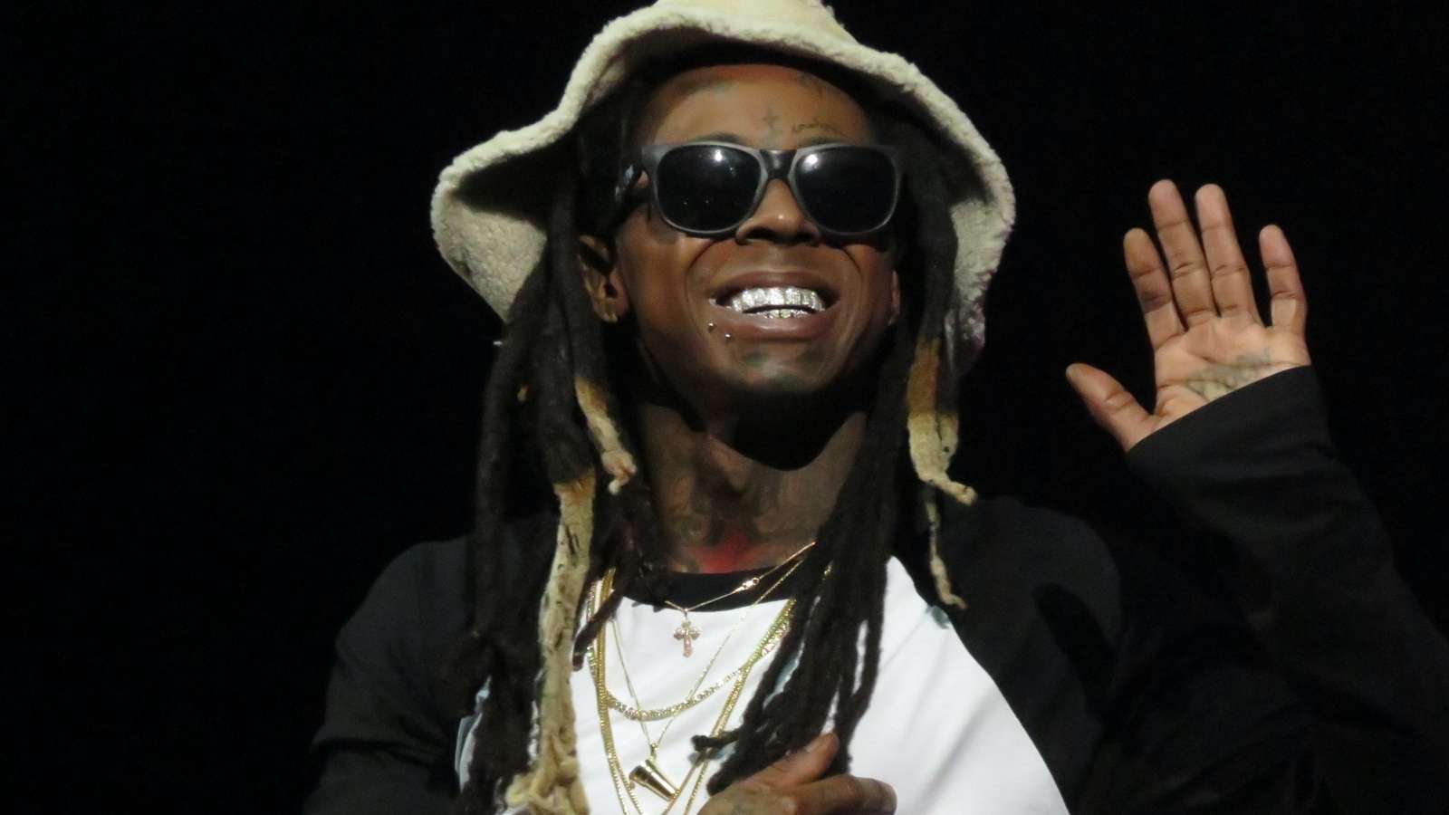 Lil Wayne smiling and waving while performing onstage at a concert.