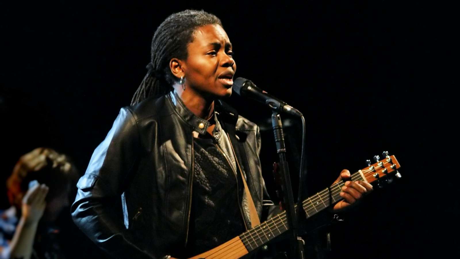 Tracy Chapman performing onstage at a concert with a guitar.
