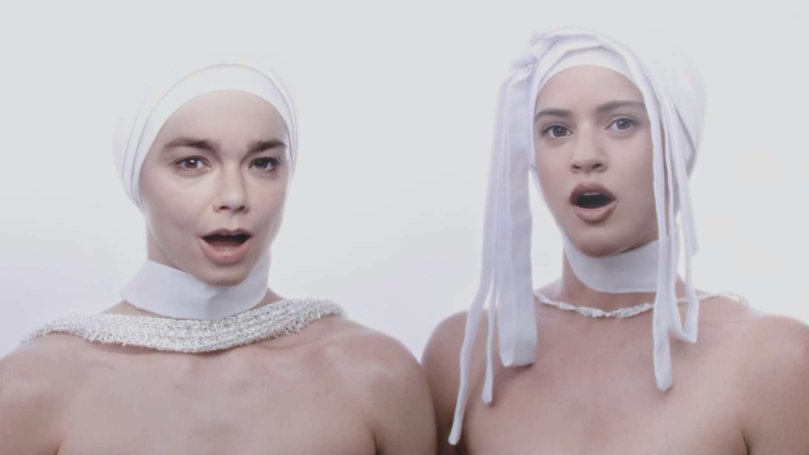 Björk and Rosalía in white outfits and headdress looking at the camera