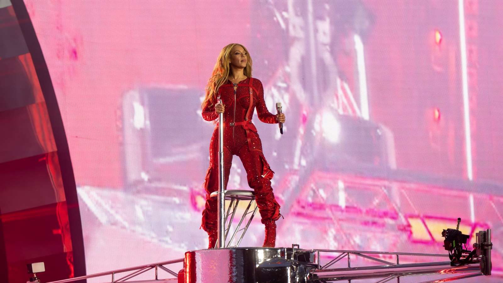 Beyonce perfomring in a red jumpsuit on a stage in concert in front of a pink backdrop