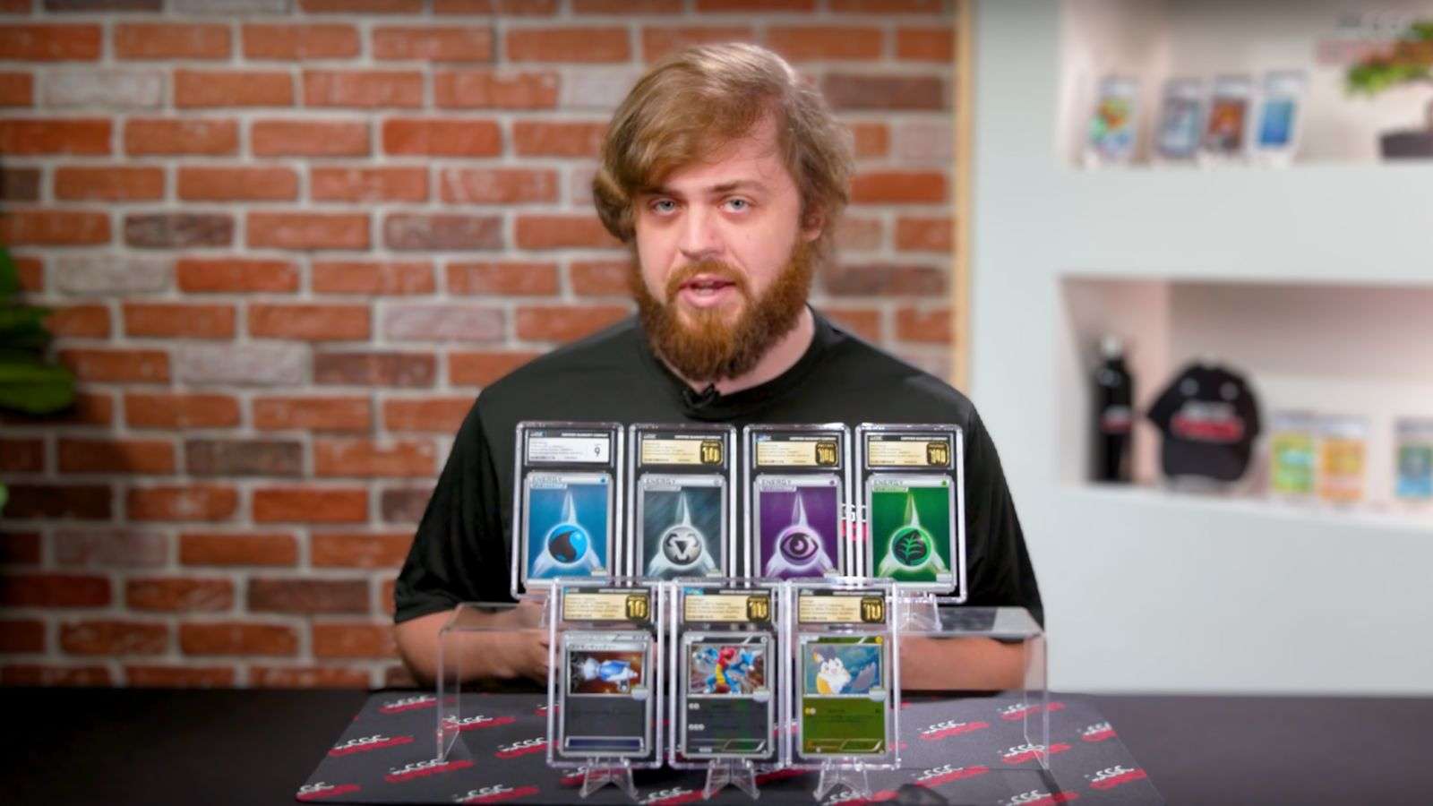 Kevin Murphy of CGC standing over a set of previously unreleased, pristine graded Pokemon cards from the 2011 Japanese World Qualifiers, including Japanese Emolga, Druddigon, Pokemon Catcher, Grass, Water, Psychic and Metal energy Pokemon and Trainer cards.