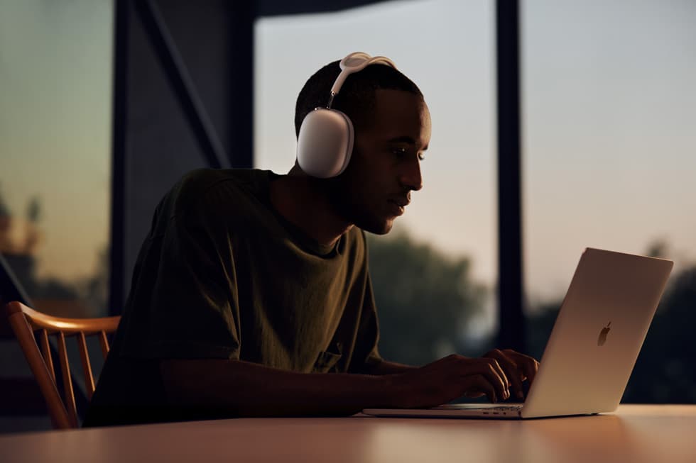 Man wearing AirPods Max while working on MacBook