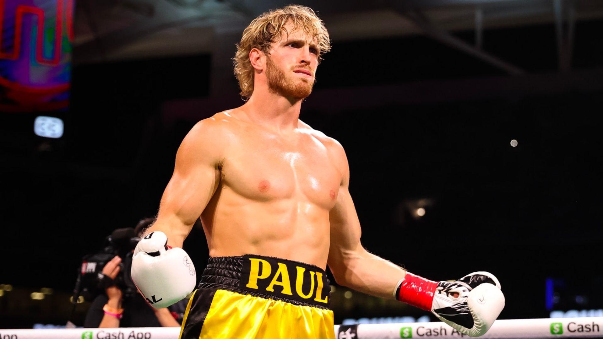 Logan Paul posing in boxing ring with white gloves and yellow trunks