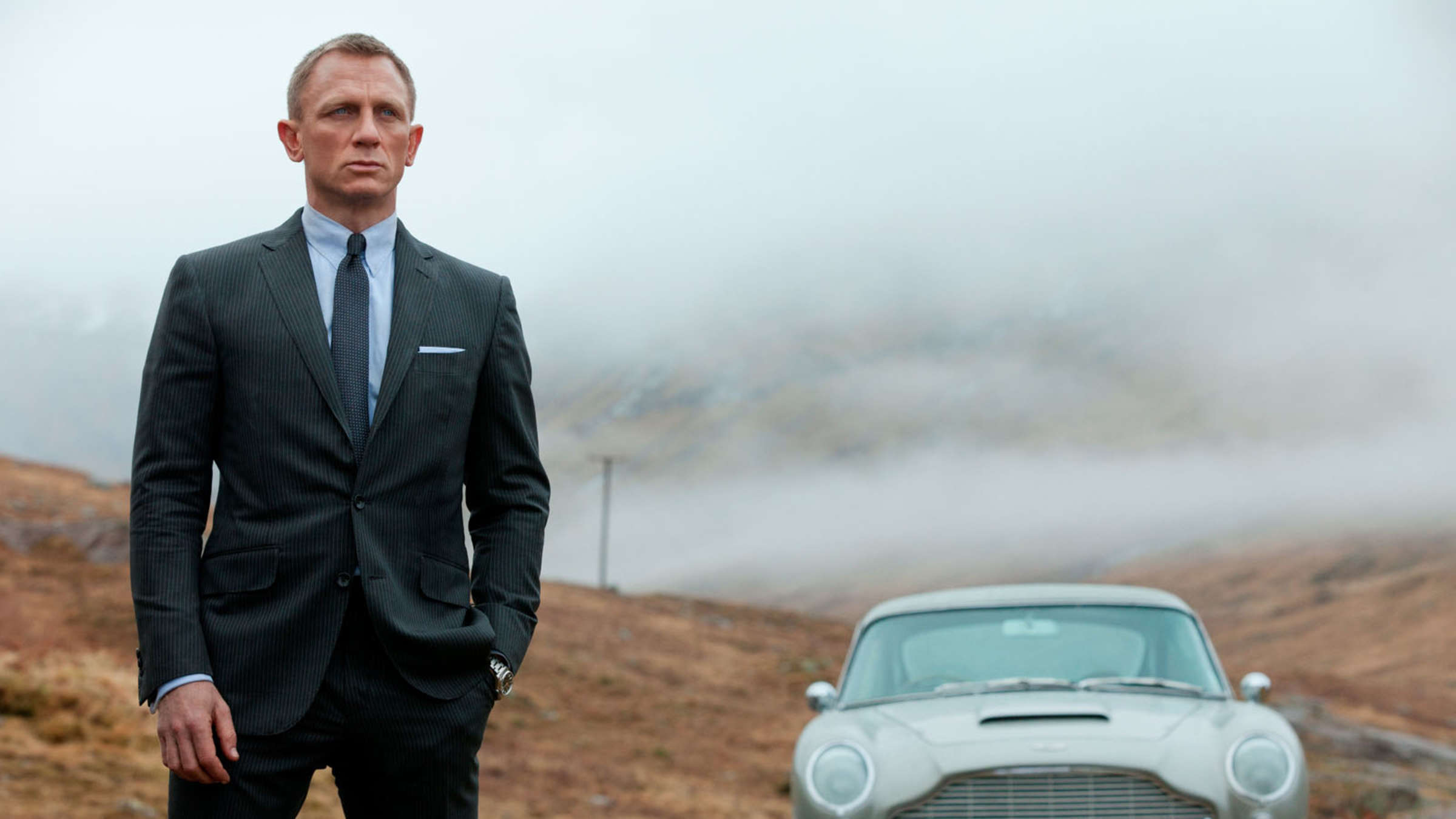 Daniel Craig as James Bond next to his classic Aston Martin in Skyfall.