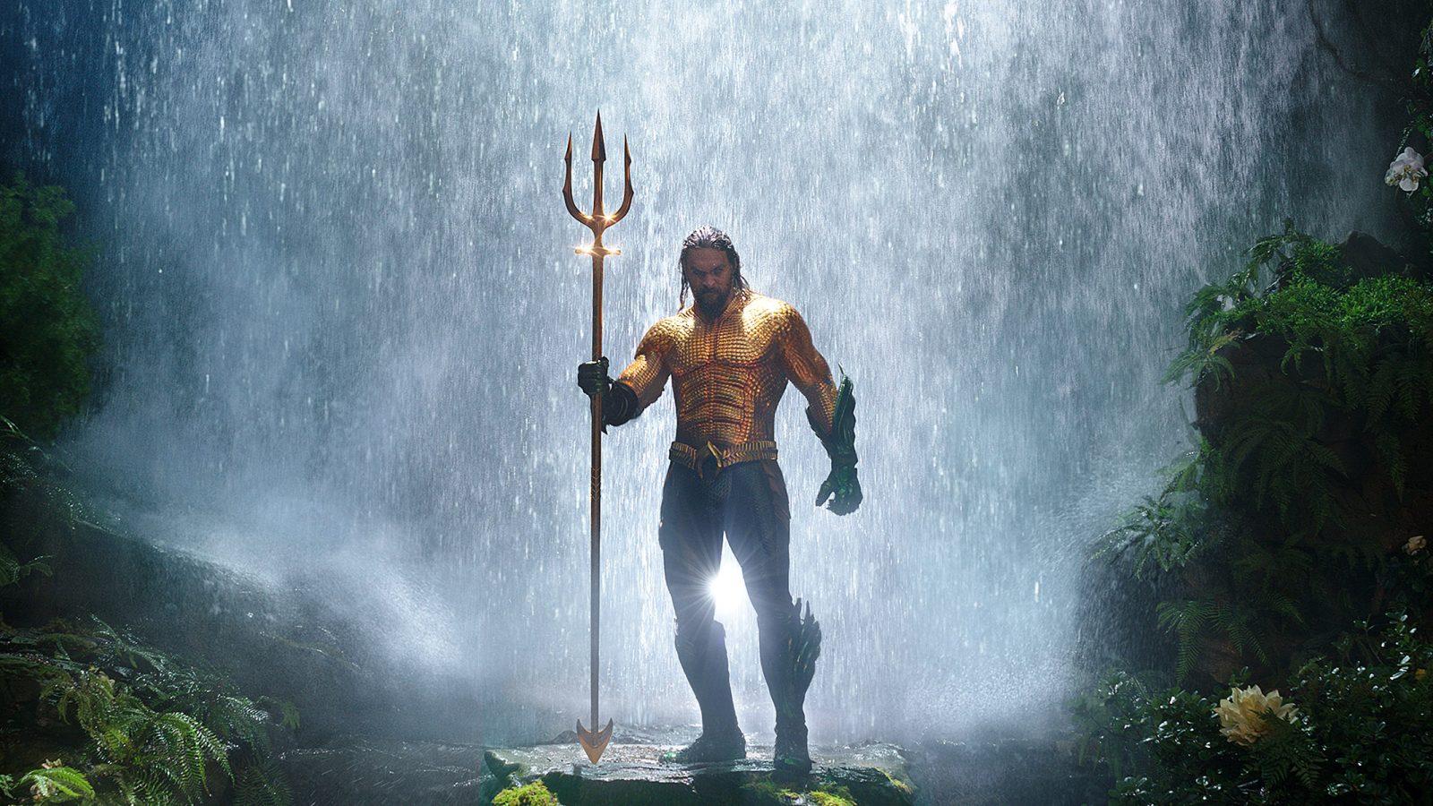Jason Momoa as Aquaman holding a trident under a waterfall in DC's Aquaman.