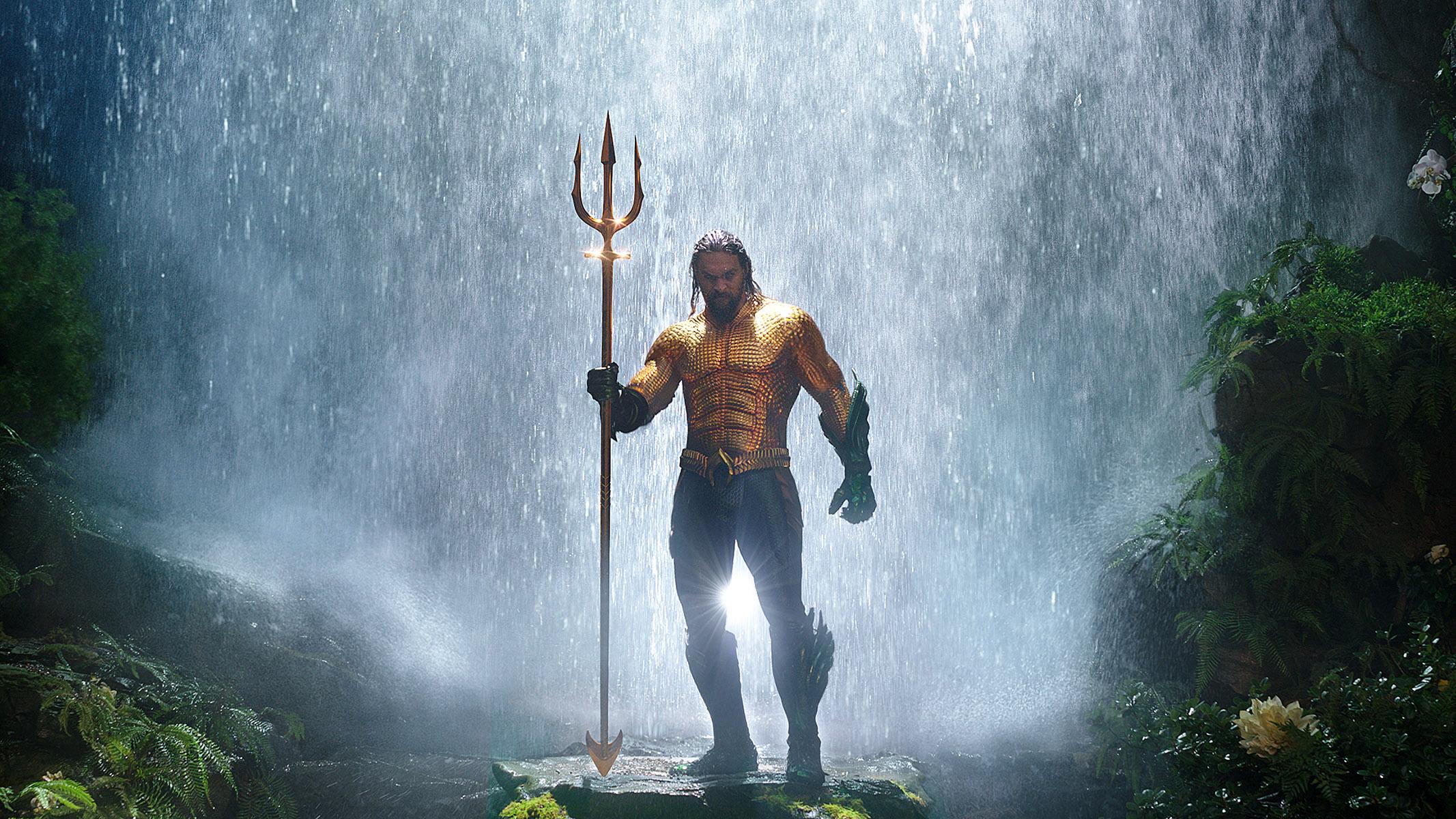 Jason Momoa as Aquaman holding a trident under a waterfall in DC's Aquaman.