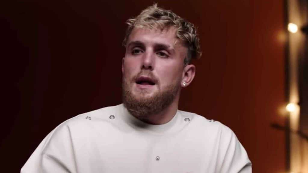 Jake Paul talking to camera in white shirt with red background and lights