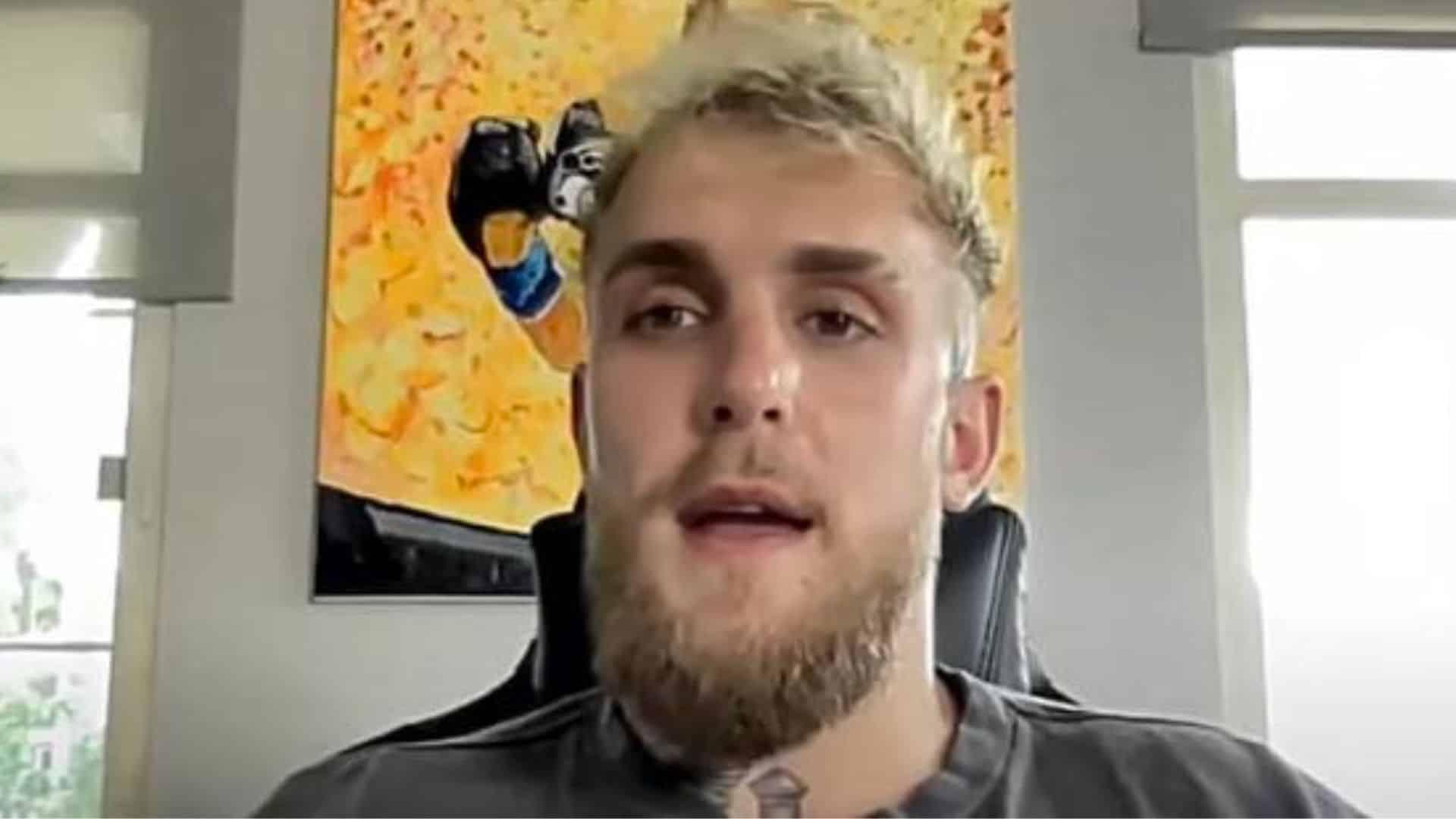 Jake Paul sitting talking to camera in front of yellow painting