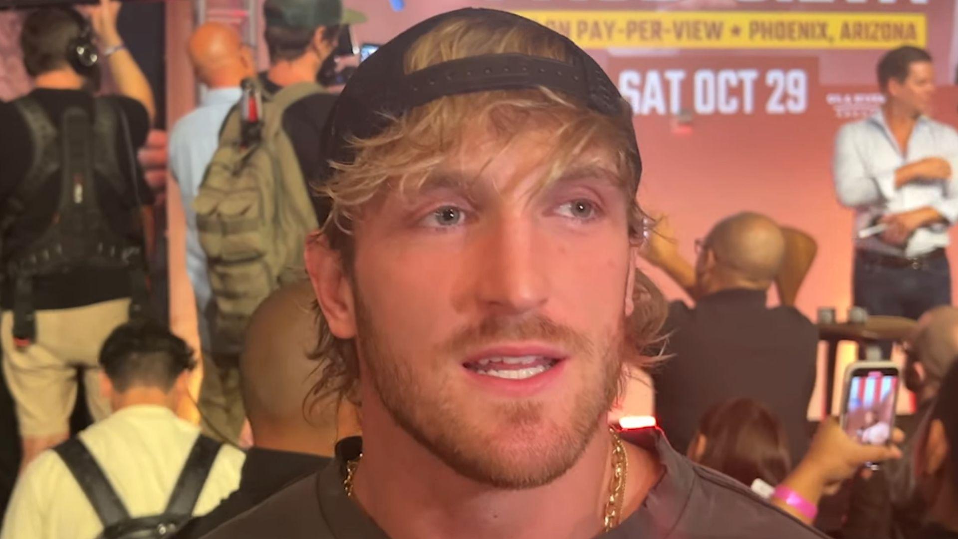 Logan Paul talking to camera with backwards hat against red background