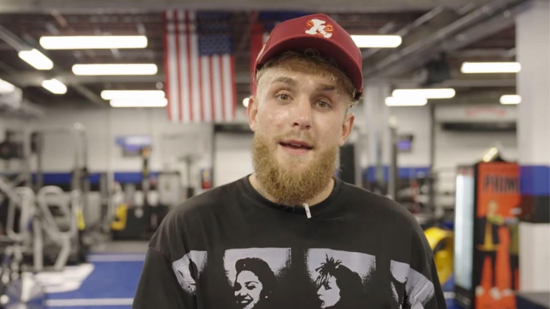 Jake Paul talking inside boxing gym with black shirt and red hat