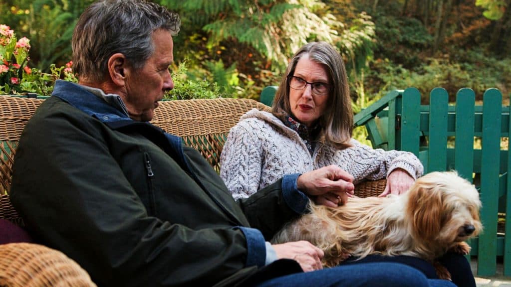 Virgin River's Hope McCrea chats to Doc on a garden bench stroking a dog.