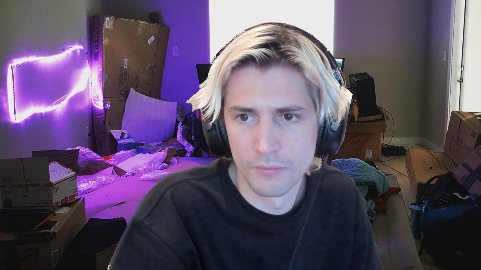 xQc with headphones sitting in a gaming chair during his stream edited onto a photo of his very first streaming setup consisting of boxes and an air mattress.