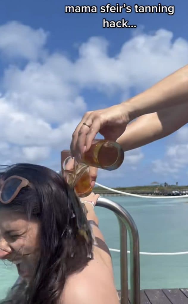 mother pours beer over daughter's shoulders to increase her tan