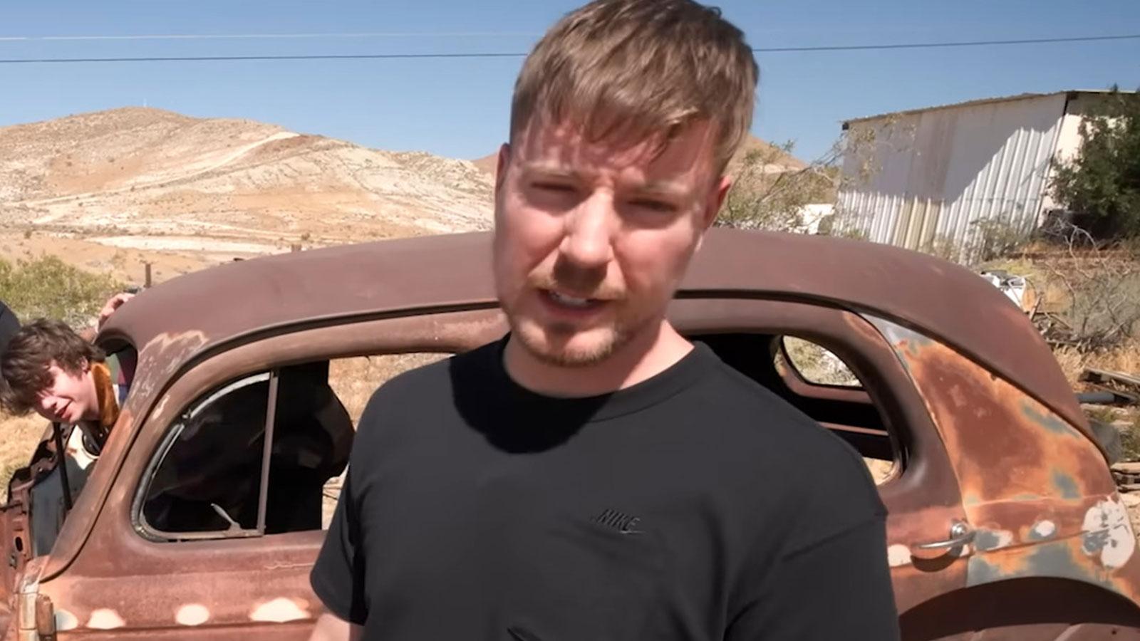 MrBeast standing in front of rusty old car