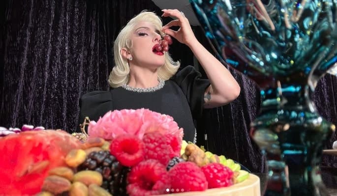 Pop singer Lady Gaga wears a black dress and puts grapes in her mouth.