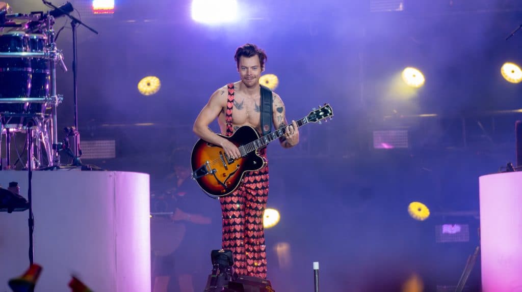 Harry Styles with a guitar performs onstage at a concert