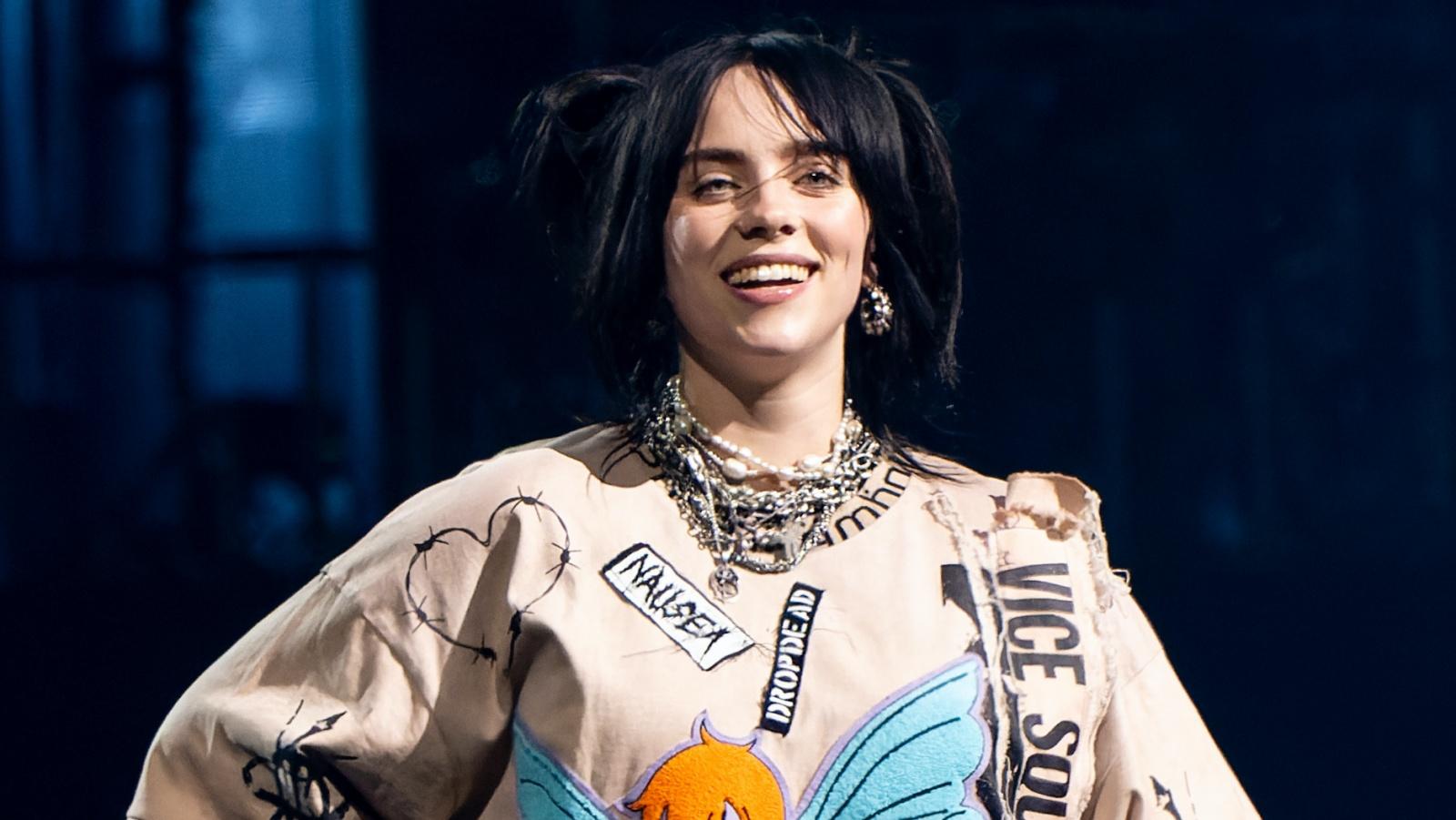 Billie Eilish with a graffiti shirt standing onstage in a concert