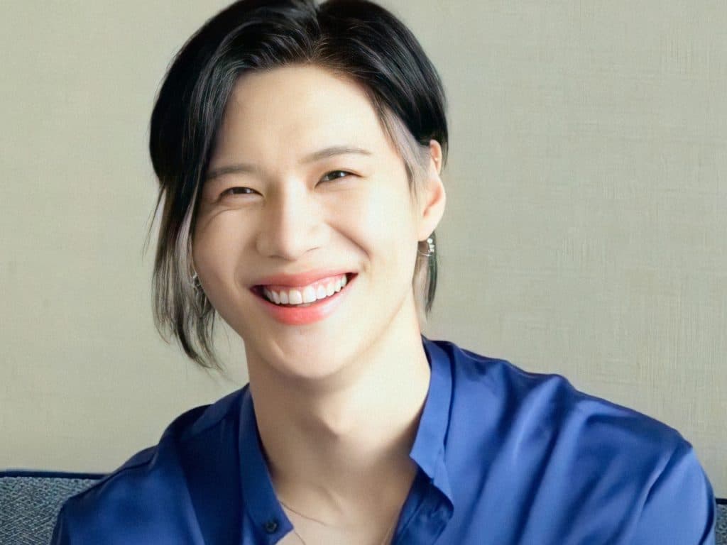 Taemin smiling in a blue button up shirt while sitting on a sofae