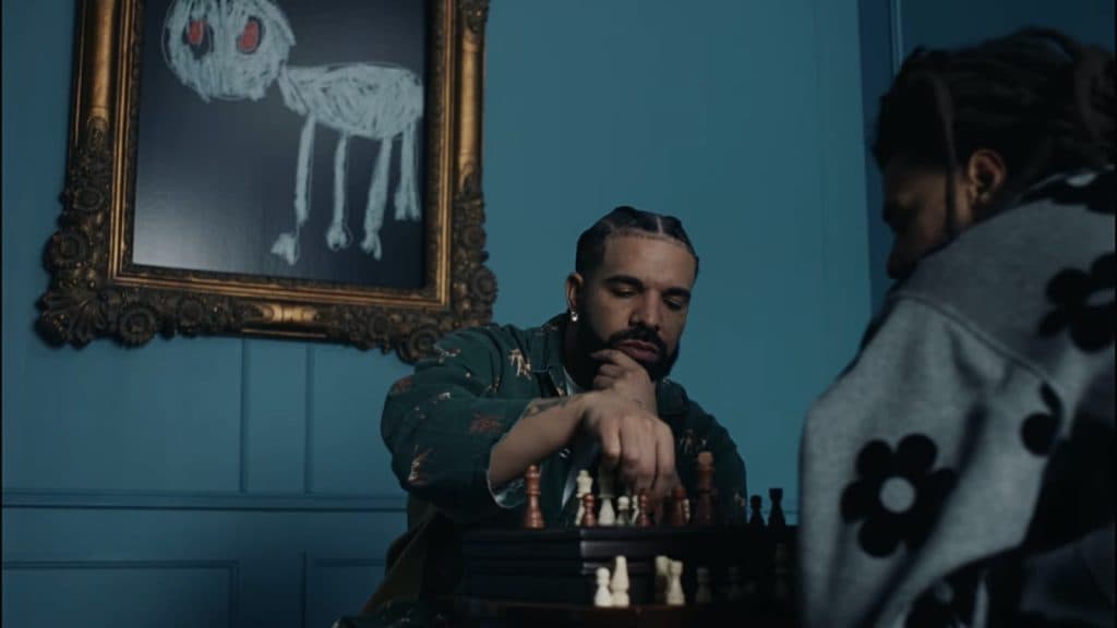 Drake and J Cole play chess in front of a teal wall