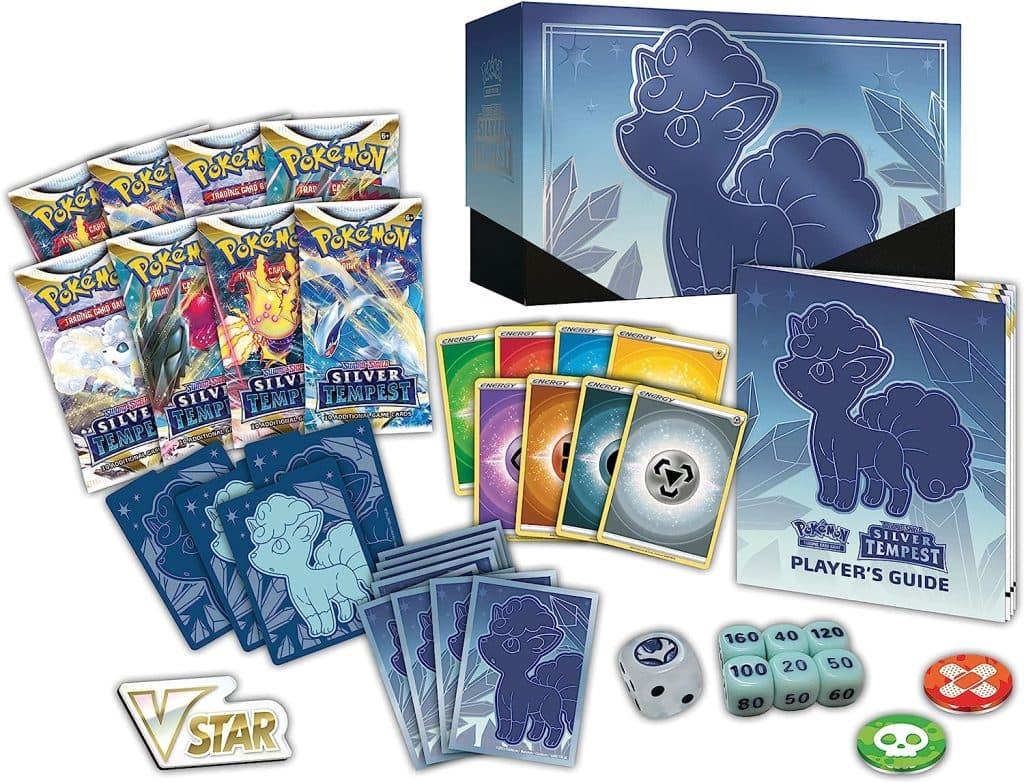A blue box with an Alolan Vulpix design stands by Pokemon card packs, coins, damage counters, dice, coins, energy cards and sleeves featuring Alolan Vulpix.