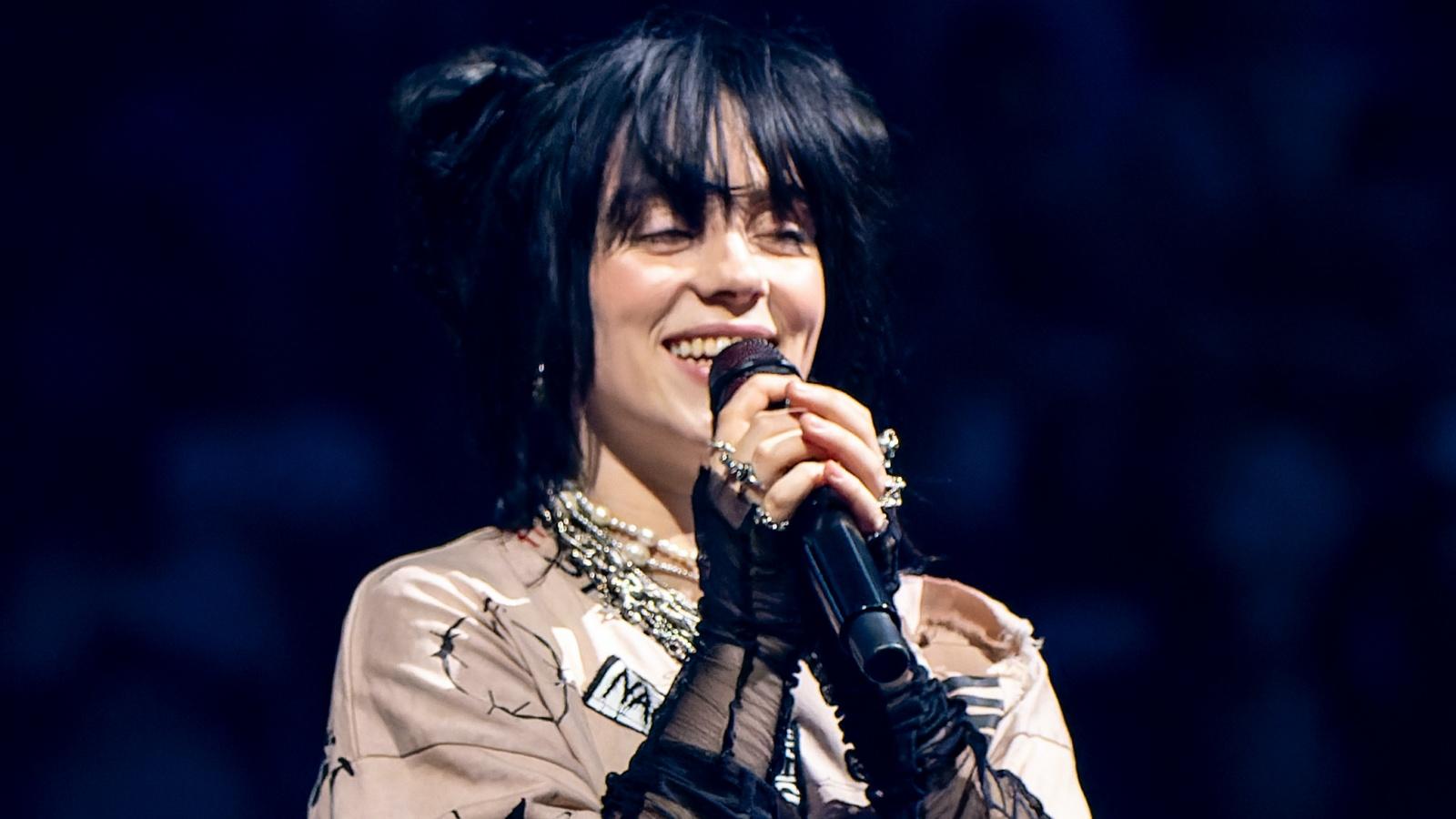 Billie Eilish smiling and holding a microphone onstage