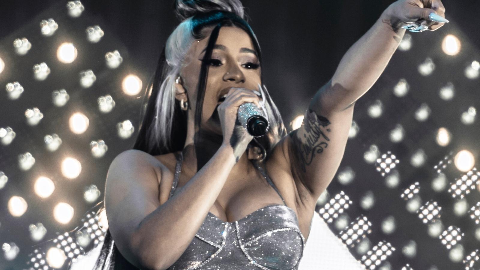 Cardi performing with an arm raised while performing onstage