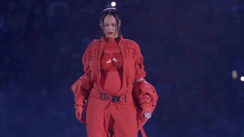 Rihanna in a bright red jumpsuit performing on a suspended platform