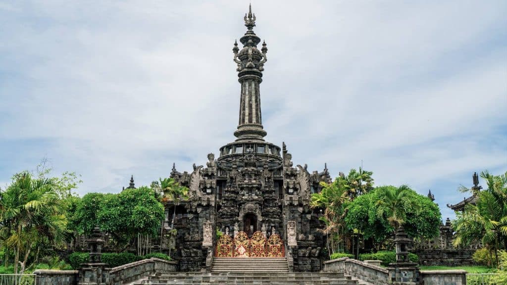 A photograph shows the Indonesian landmark, Kawasan Lapangan Puputan Margarana, Niti Mandala Denpasar. It is a large temple with a spire, and gates made of brightly colored metals