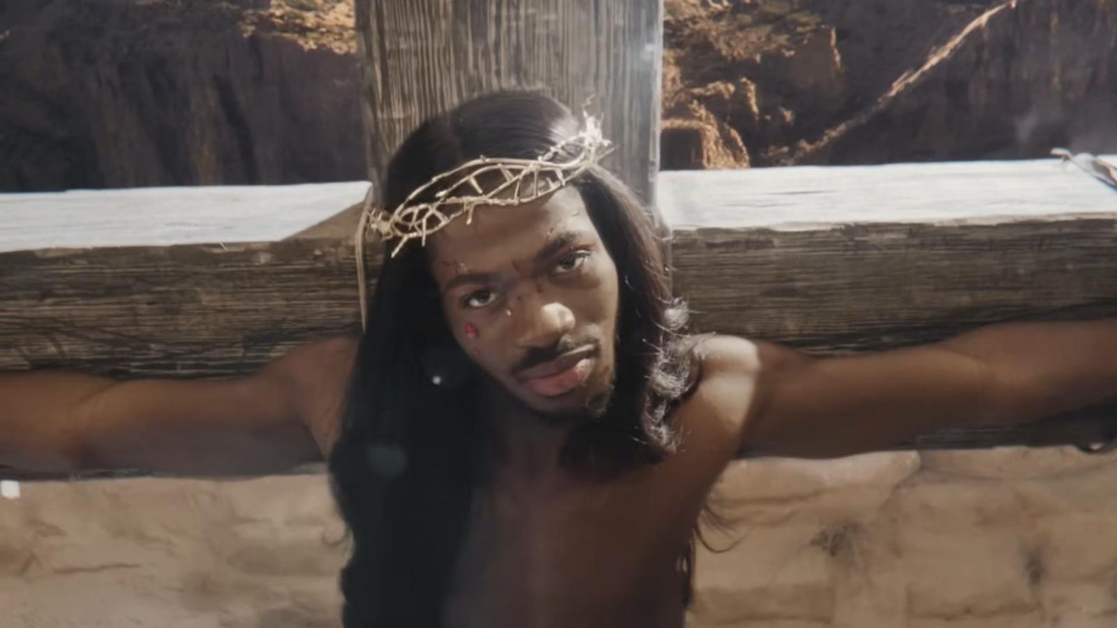 Lil Nas X wearing a crown and hanging on a cross
