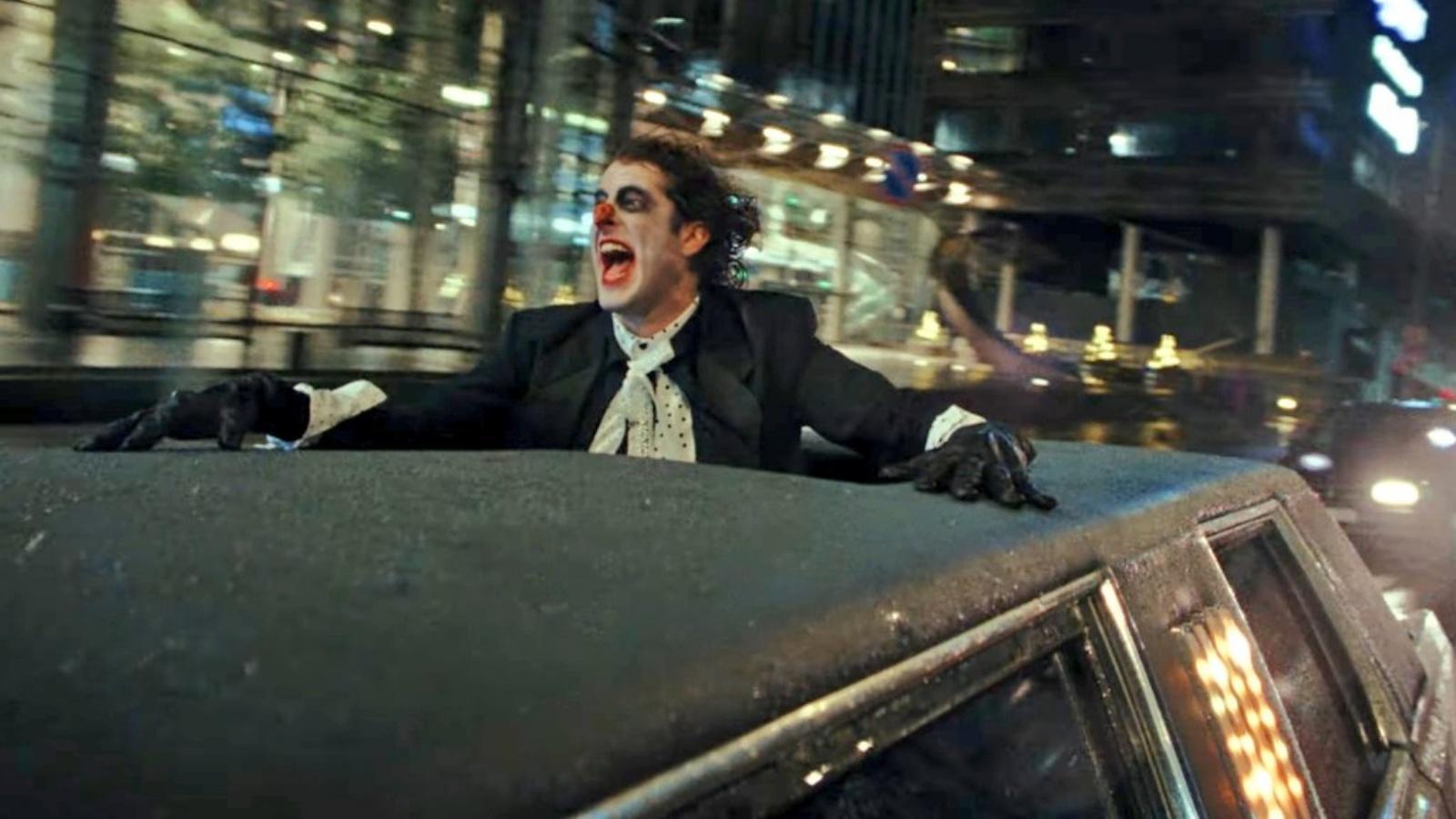 Lil Dicky dressed up like the Joker hanging out of a limo rooftop