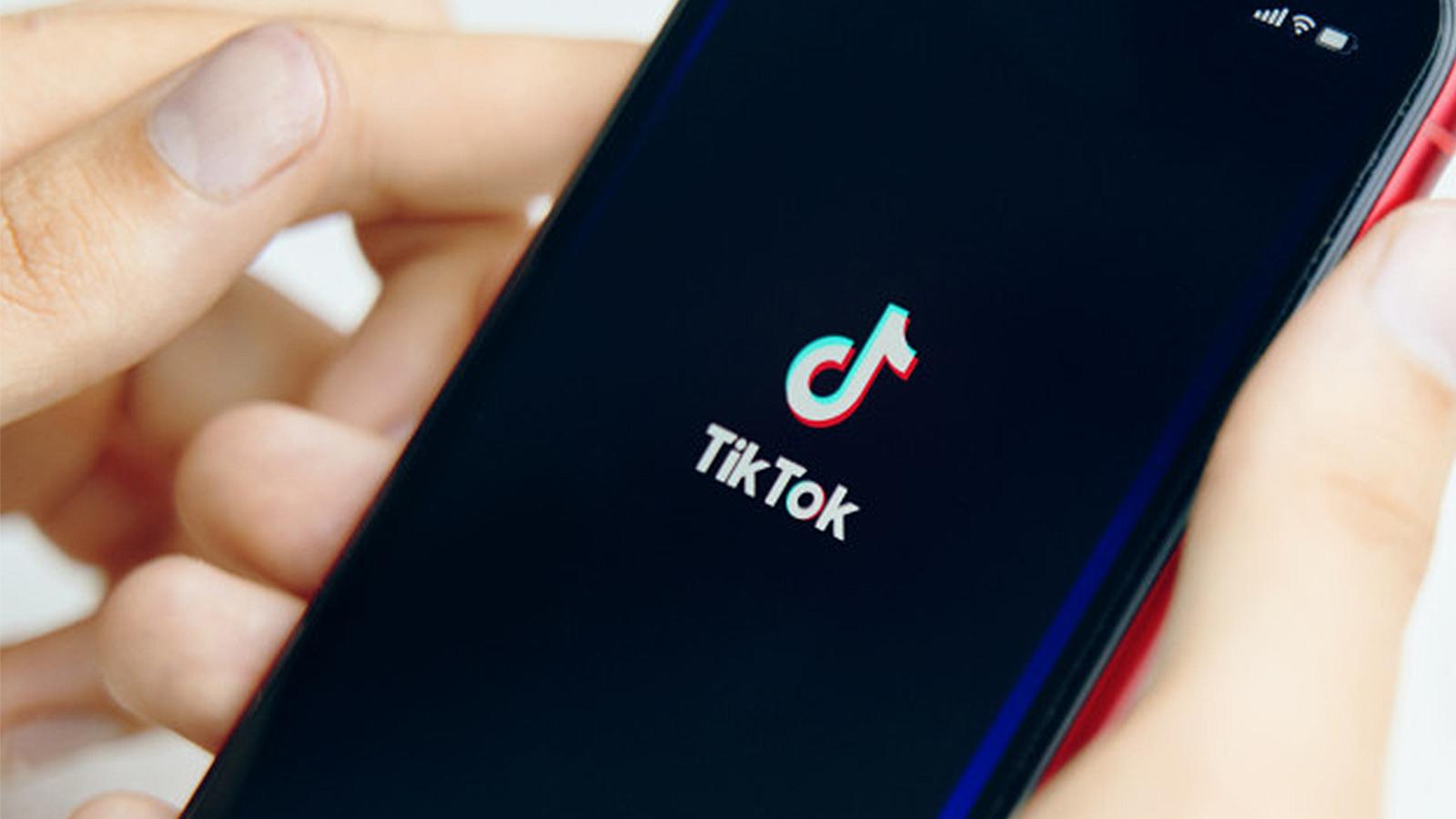 A smartphone with the TikTok logo is held in a person's hand.