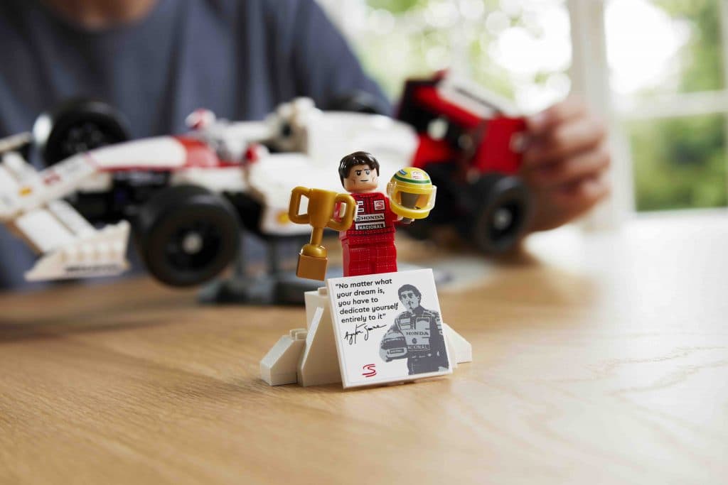 The Aryton Senna minifigure included with the LEGO Icons McLaren MP4/4 set displayed on a stand with accessories.