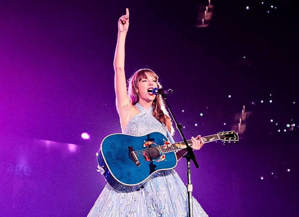Taylor Swift performing with a teal guitar onstage at an Eras Tour concert