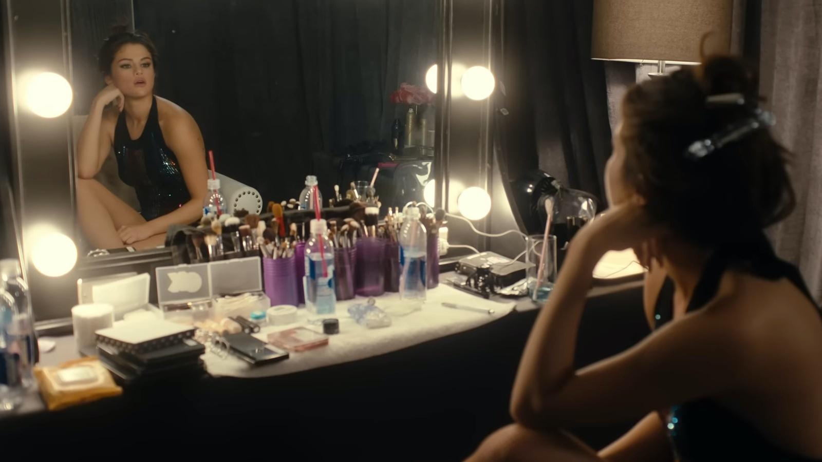 Selena Gomez staring into a lit-up mirror backstage