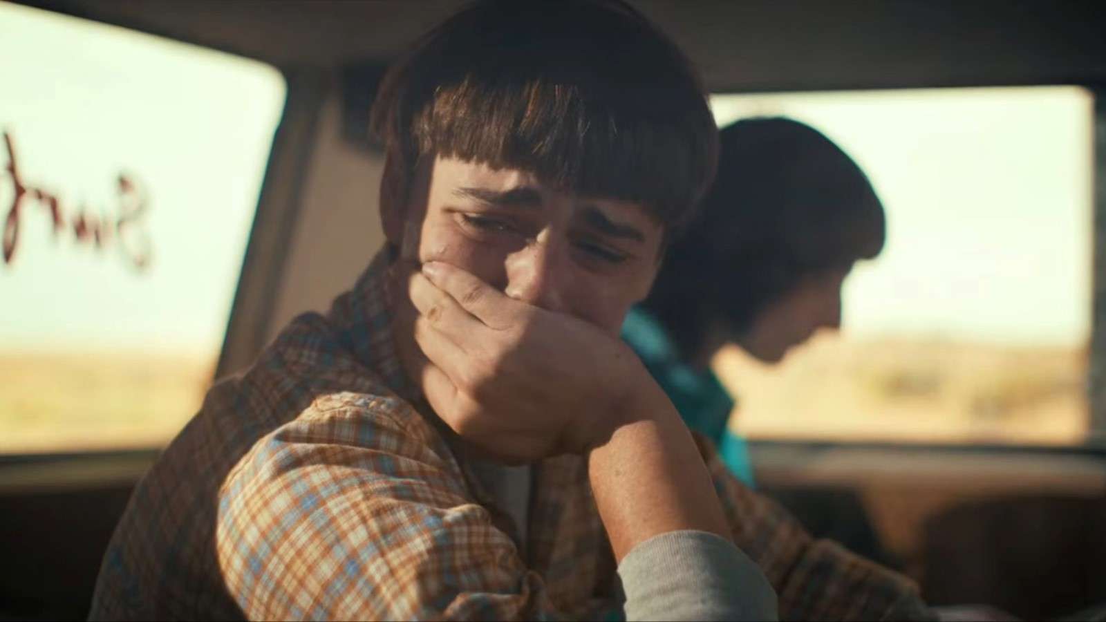 Will in Stranger Things looking out the car window and crying, his hand pressed to his face