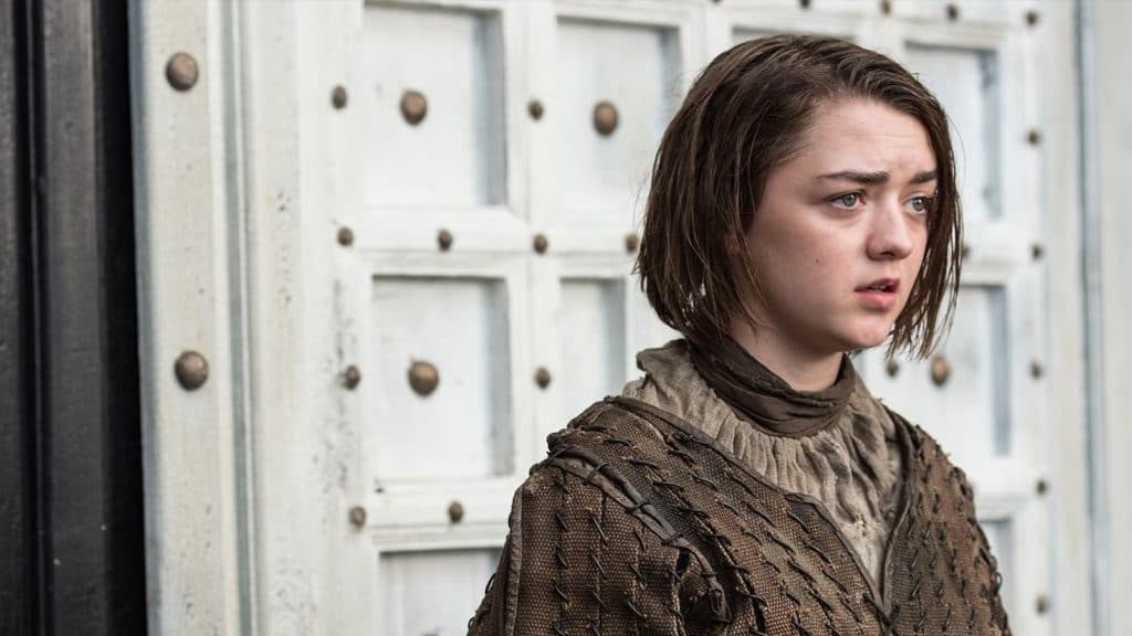 Maisie Williams as Arya Stark in Game of Thrones standing by a door and looking out