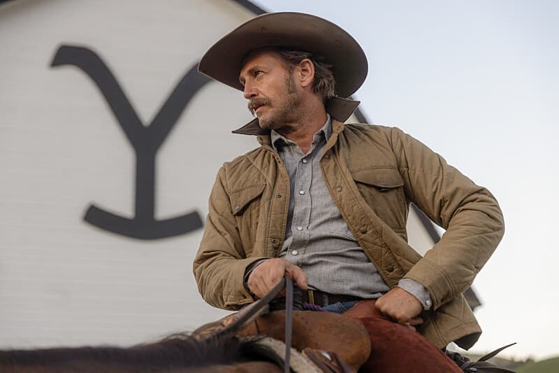 Josh Lucas as Young John Dutton sitting on a horse with the Yellowstone logo in the background