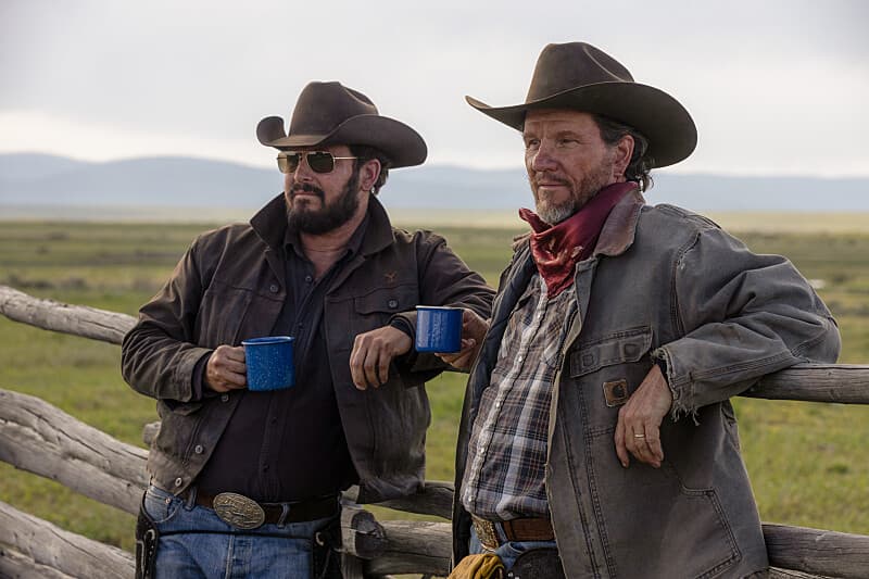 Two cowboys leaning against a fence and drinking coffee in Yellowstone